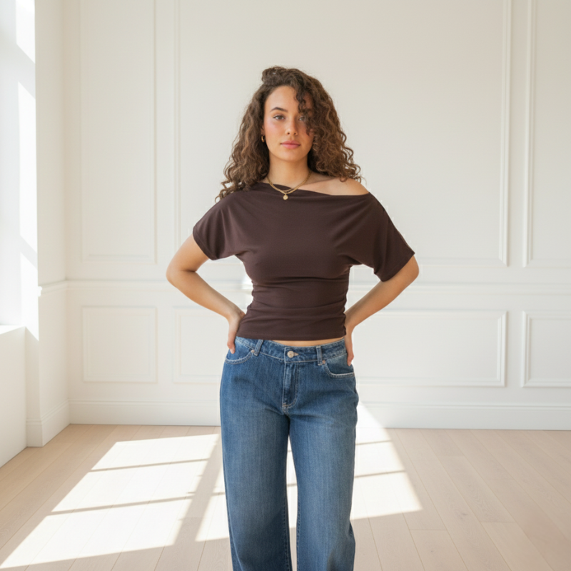 Model trägt ein braunes, figurbetontes Top kombiniert mit Jeans in einer hellen Innenraumszene.