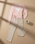 Rosa Wickeltop und beige Hose als Flatlay arrangiert auf hellem Hintergrund mit weichen Schatten und minimalistischer Präsentation.