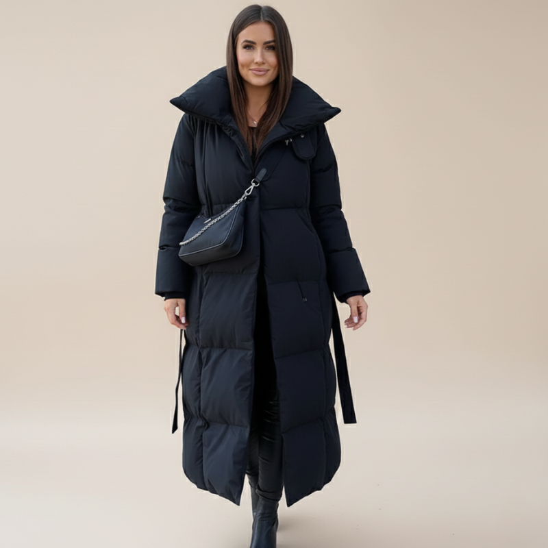Model trägt einen langen schwarzen Wintermantel mit breitem Kragen, Gürtel und gestepptem Design im Studio.