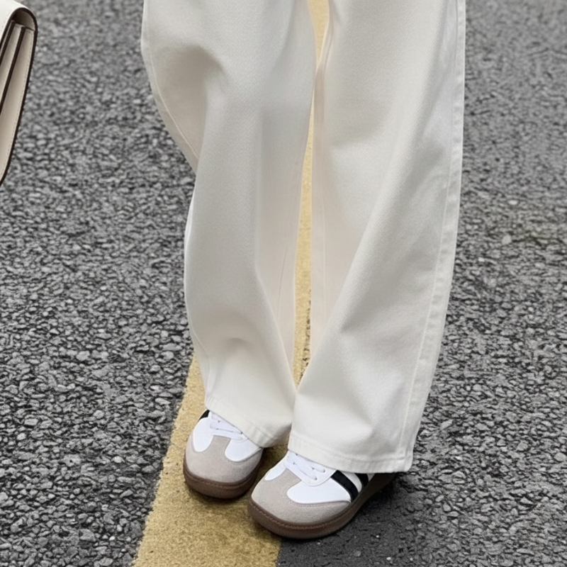 Nahaufnahme der weißen Stoffhose mit weitem Bein und hellen Schuhen auf strukturiertem Boden.