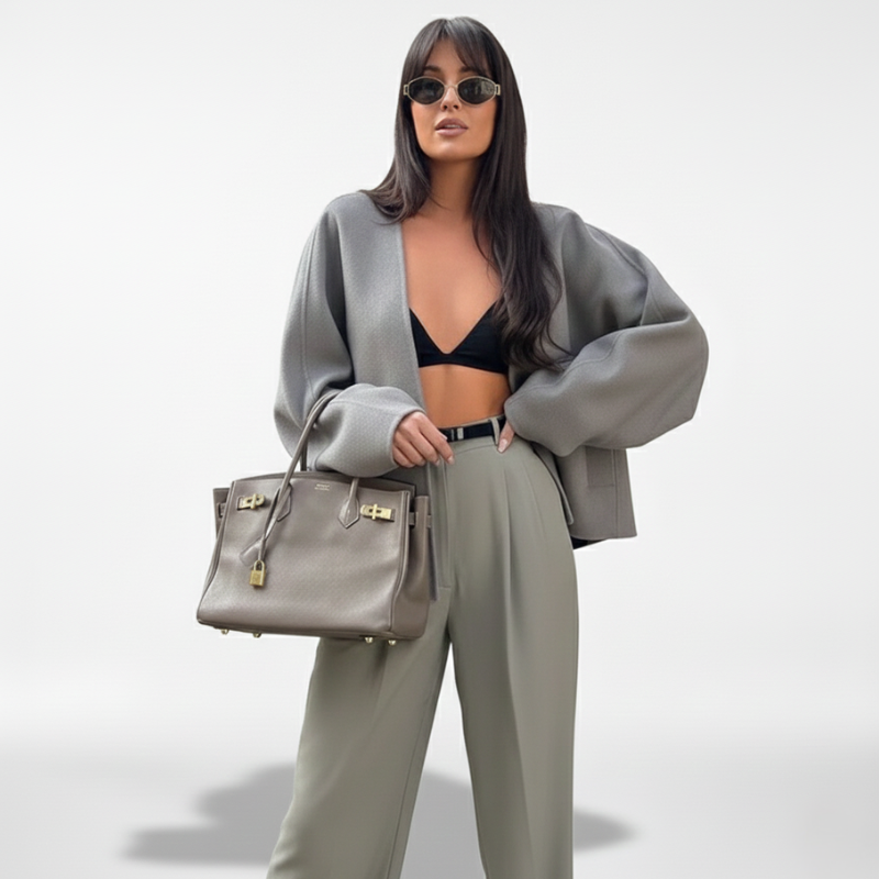 Frau posiert in grauer Jacke und weiter grauer Hose, aufgenommen in einem hell ausgeleuchteten Innenraum.