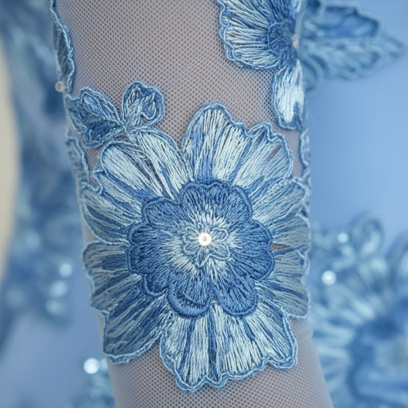 Nahaufnahme der blauen Blumenstickerei mit feiner Textur und dekorativen Blütenelementen auf transparentem Stoff.