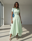 Model trägt ein mintgrünes Maxikleid mit elegantem Faltenwurf und Kragen in einem modernen Indoor-Setting.