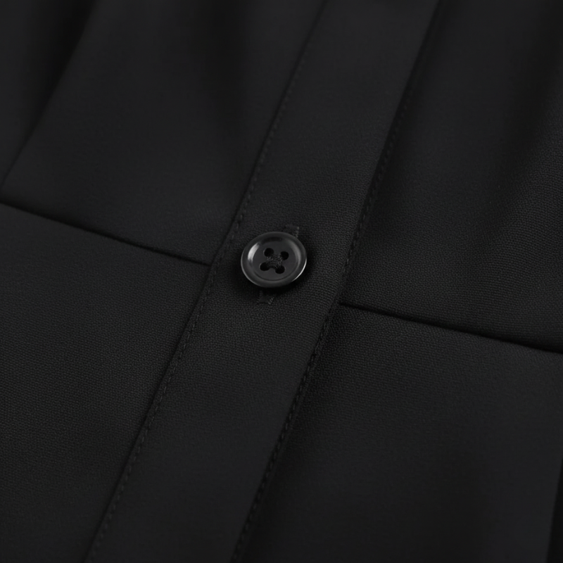 Nahaufnahme des schwarzen Kleids mit strukturiertem Stoff, präzisem Kragen und sauber verarbeitetem Knopfdetail.