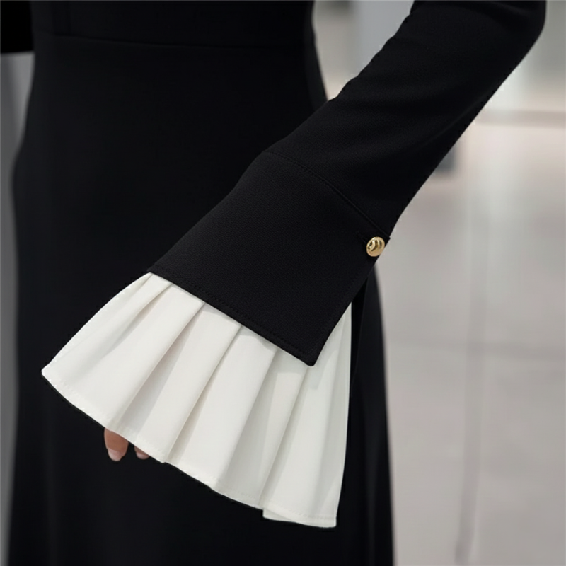 Nahaufnahme des schwarzen Kleids mit plissierten weißen Manschetten und fein strukturierter Stoffoberfläche.