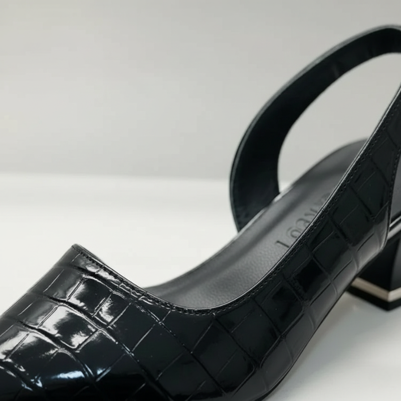 Nahaufnahme eines schwarzen Slingback-Schuhs mit strukturierter Oberfläche und mittlerem Absatz auf hellem Hintergrund.
