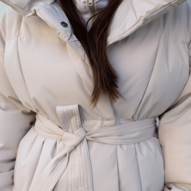 Nahaufnahme der cremefarbenen Steppjacke mit hohem Kragen, Bindegürtel und feiner Steppstruktur.